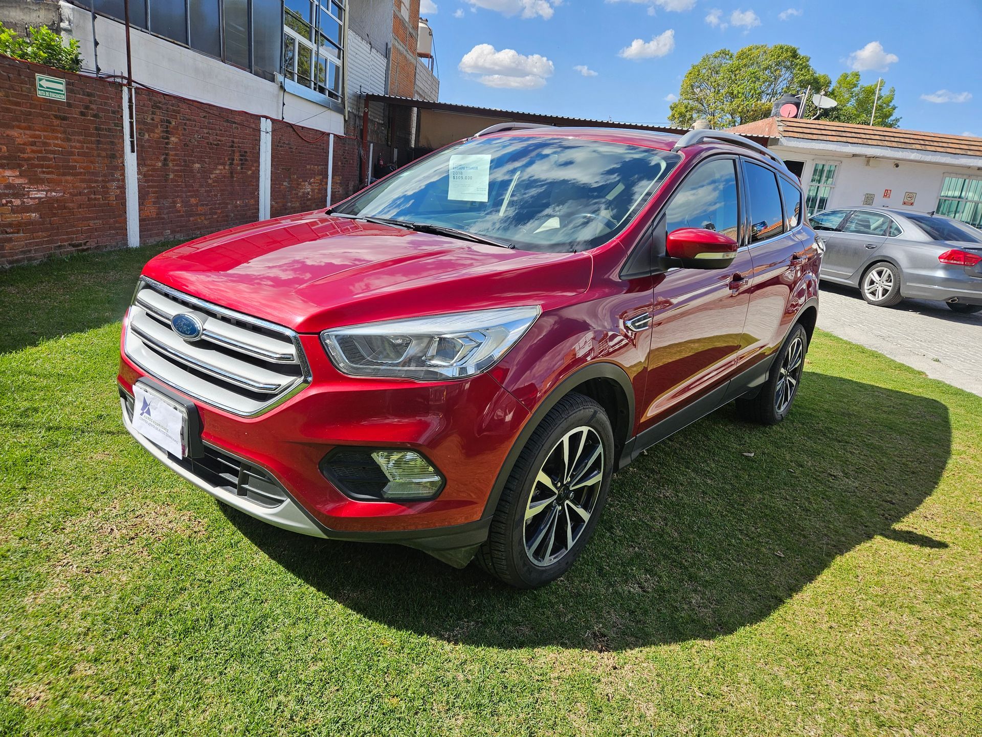 SUV Ford Escape de color rojo estacionado en el césped frente a un edificio de ladrillos.