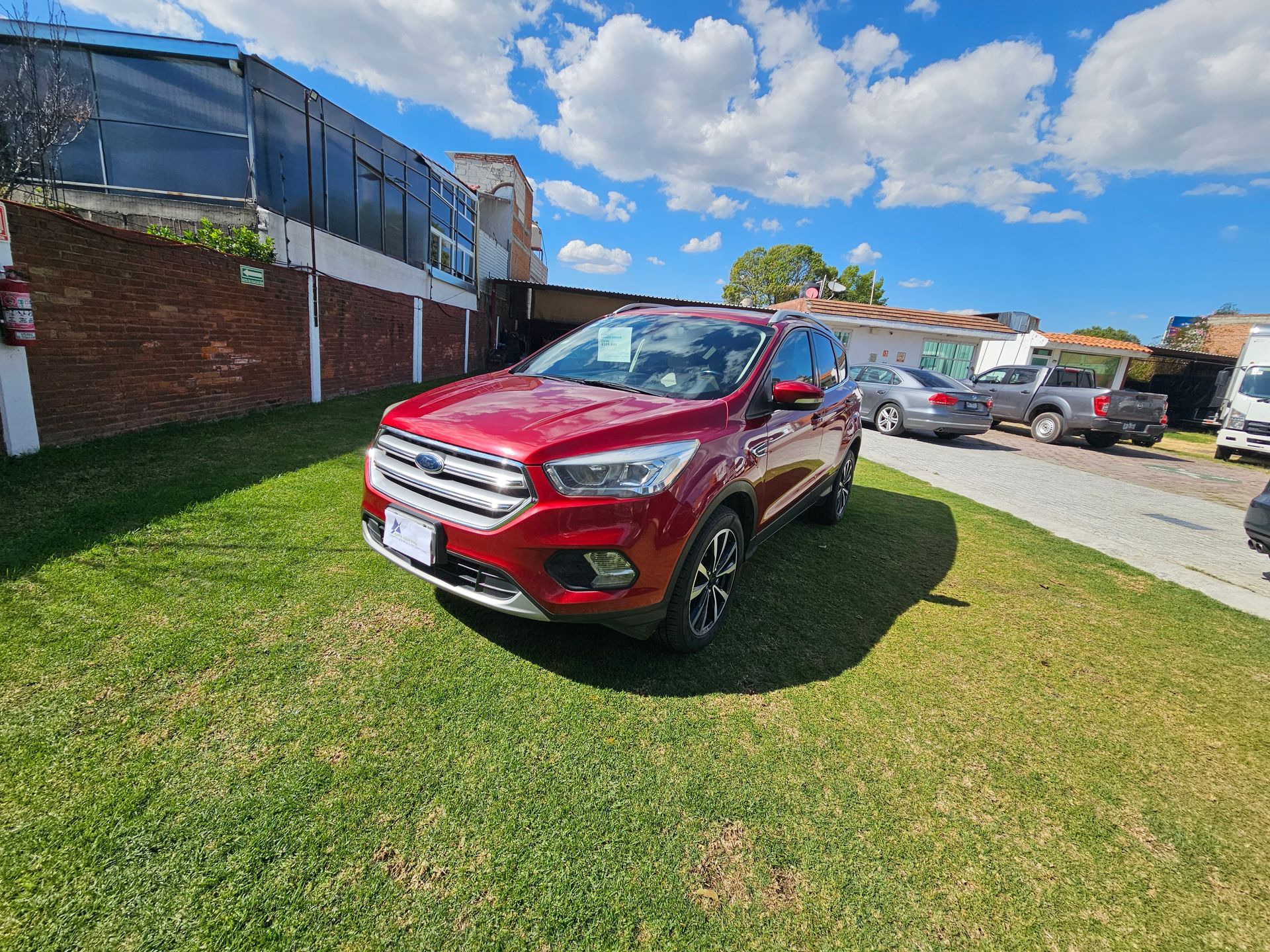 SUV Ford Escape rojo estacionado sobre césped verde, día soleado.