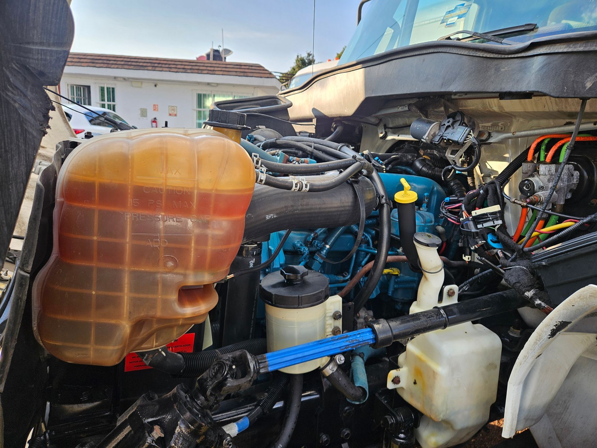 Motor de un camión International azul con depósito de refrigerante, mangueras y cableado visibles.