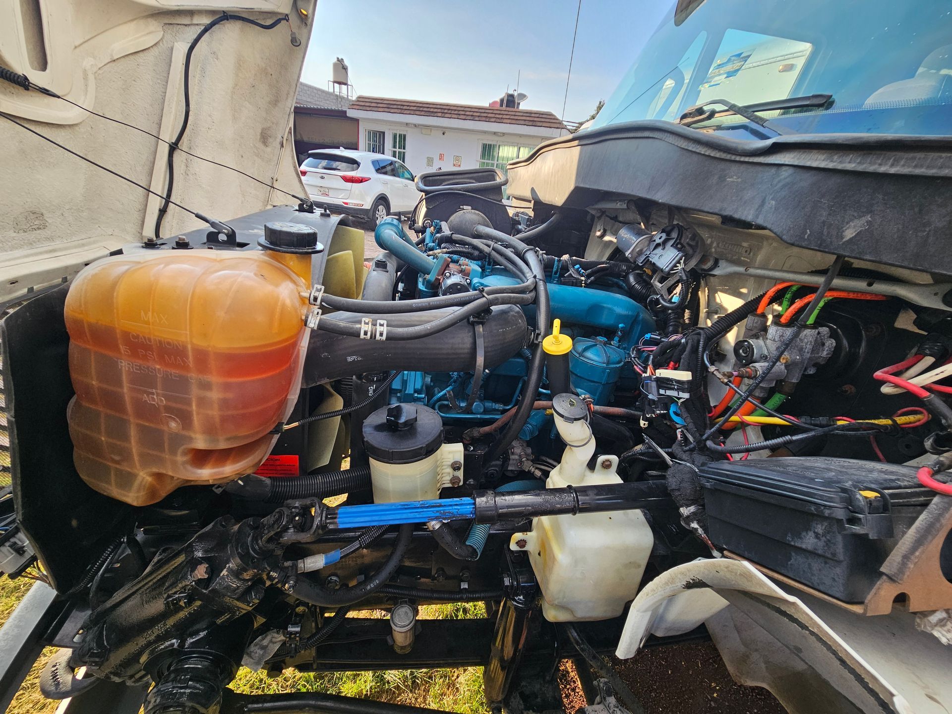 Motor de un camión azul y negro con componentes expuestos, con un depósito amarillo y naranja en foco.