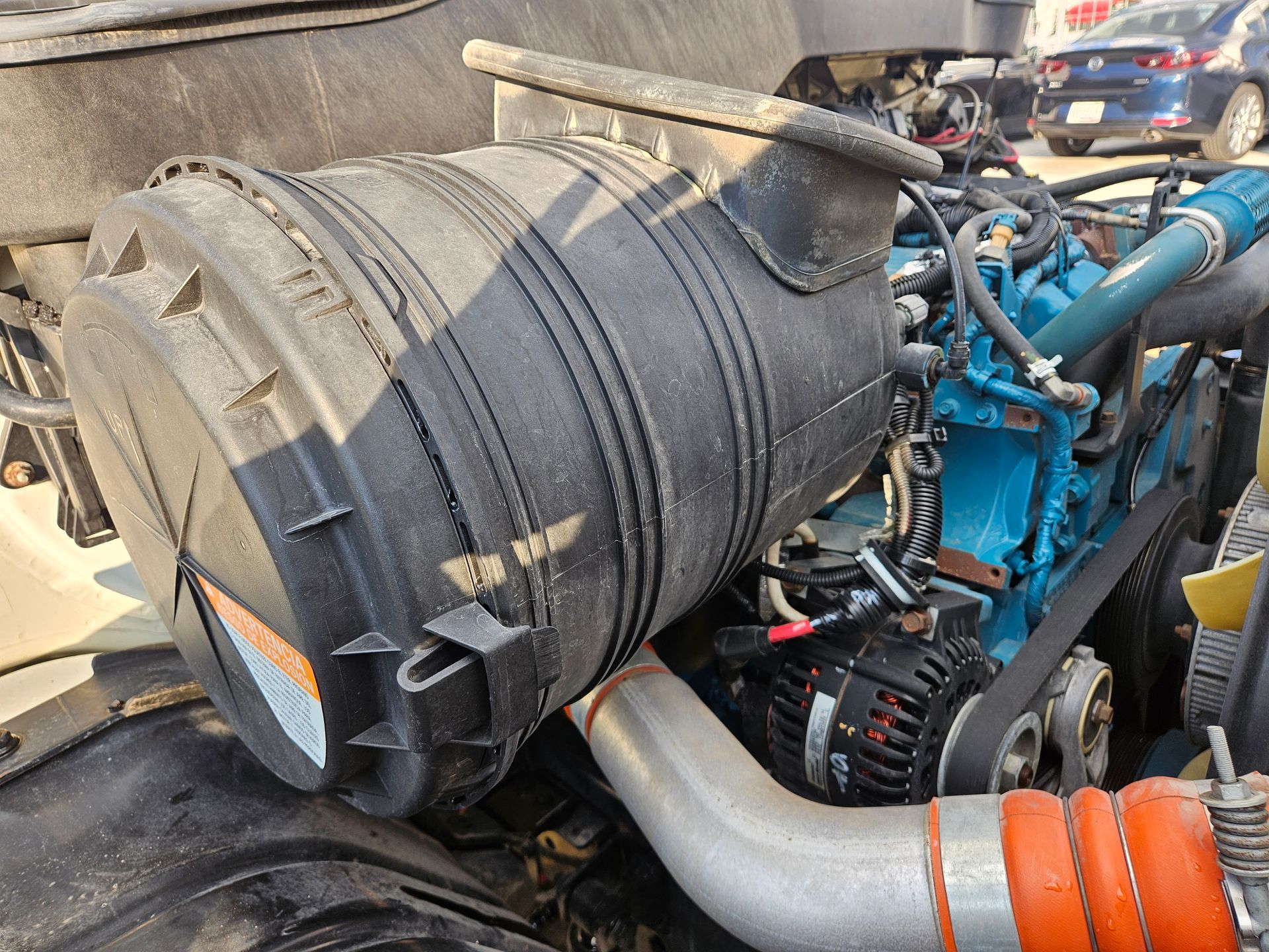 Filtro de aire negro en el motor de un camión. También se ven el motor azul y el tubo plateado.