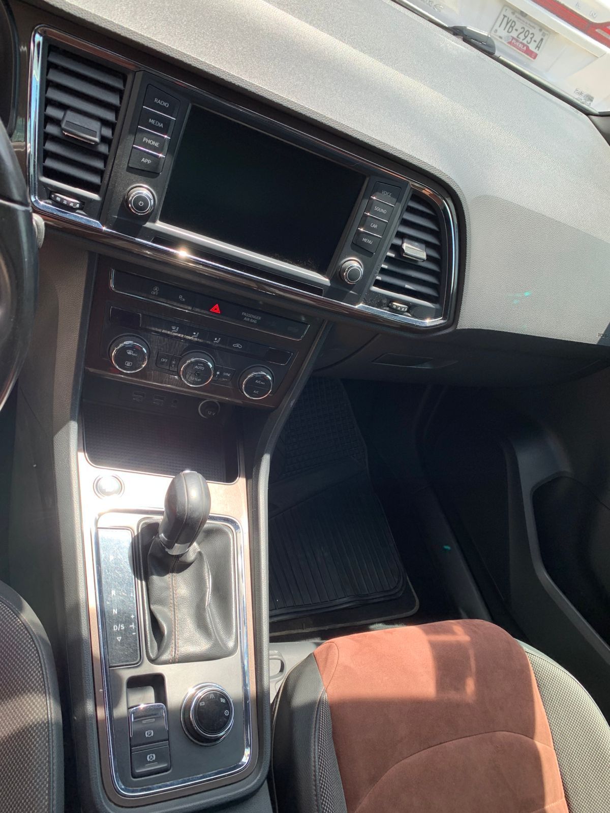 Interior del coche con consola central, pantalla táctil, palanca de cambios y asiento marrón y negro.