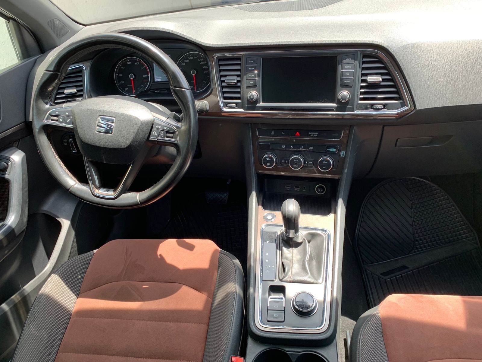 Interior del coche: tablero negro, asientos marrones, volante, pantalla multimedia, palanca de cambios y controles de aire acondicionado.