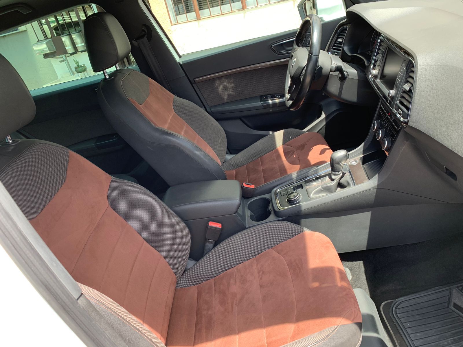Interior de un automóvil con asientos, volante y consola de color marrón y negro.