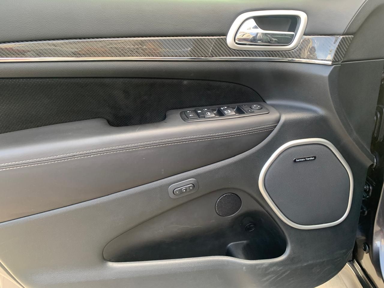 Interior de puerta de coche de color negro, con controles para altavoces, ventanas y espejos.