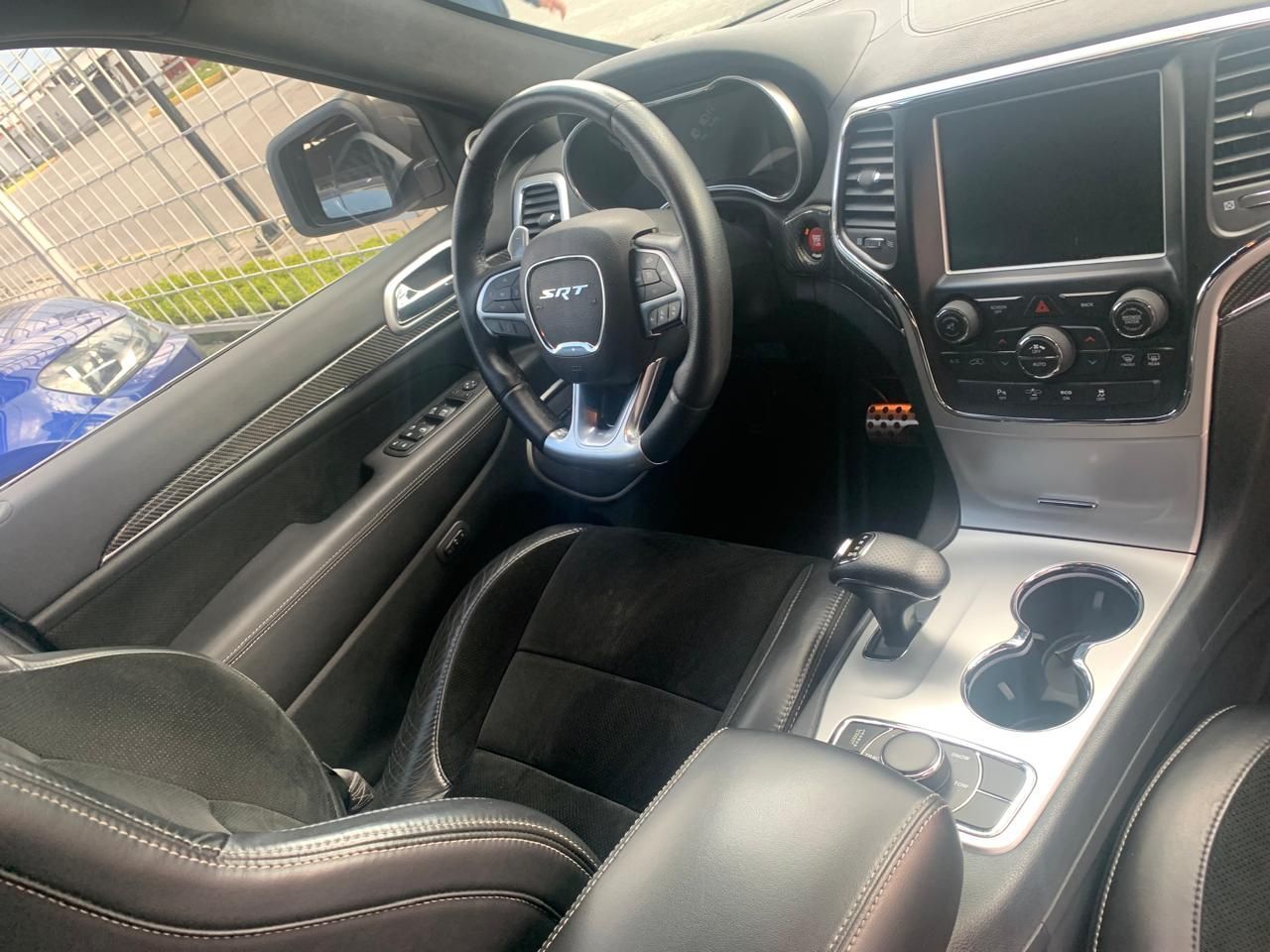 Vista interior de un automóvil negro con volante, asientos, tablero y consola.