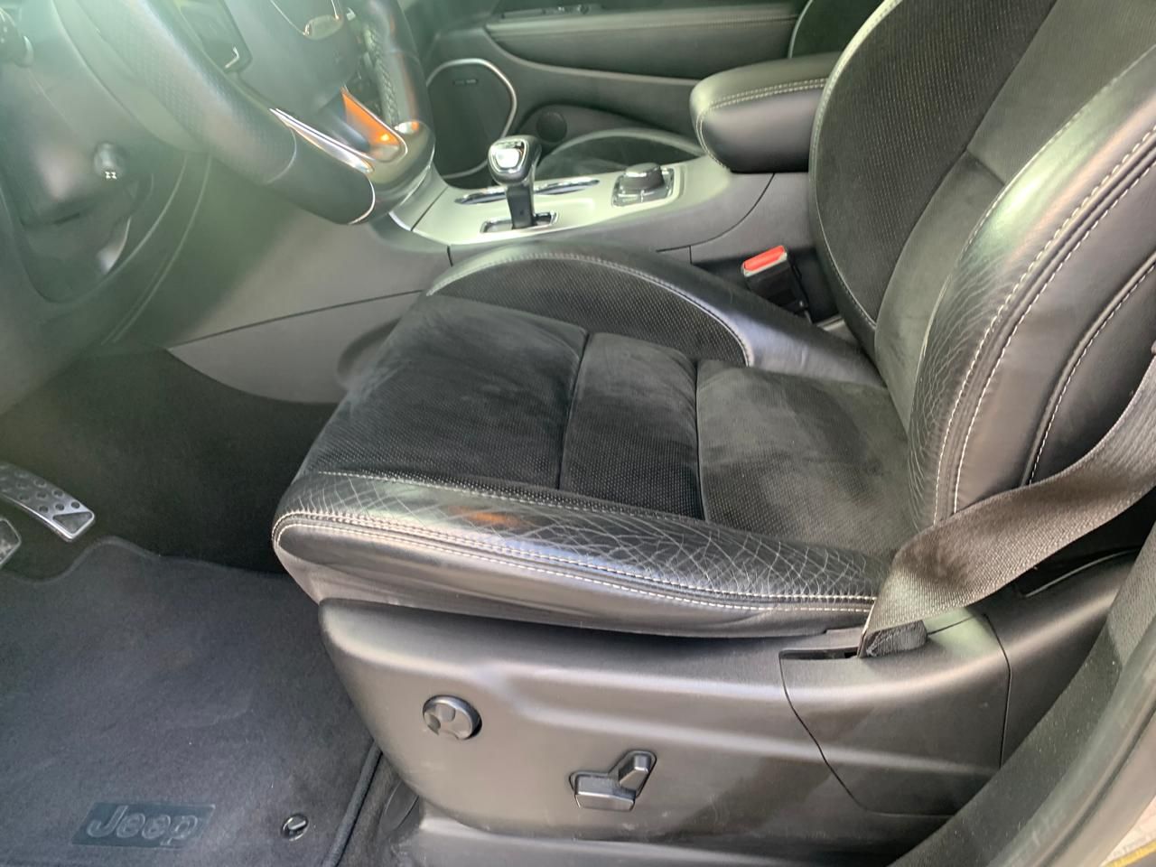 Asiento de automóvil en cuero negro con detalles de desgaste y costuras, y controles de ajuste del asiento.