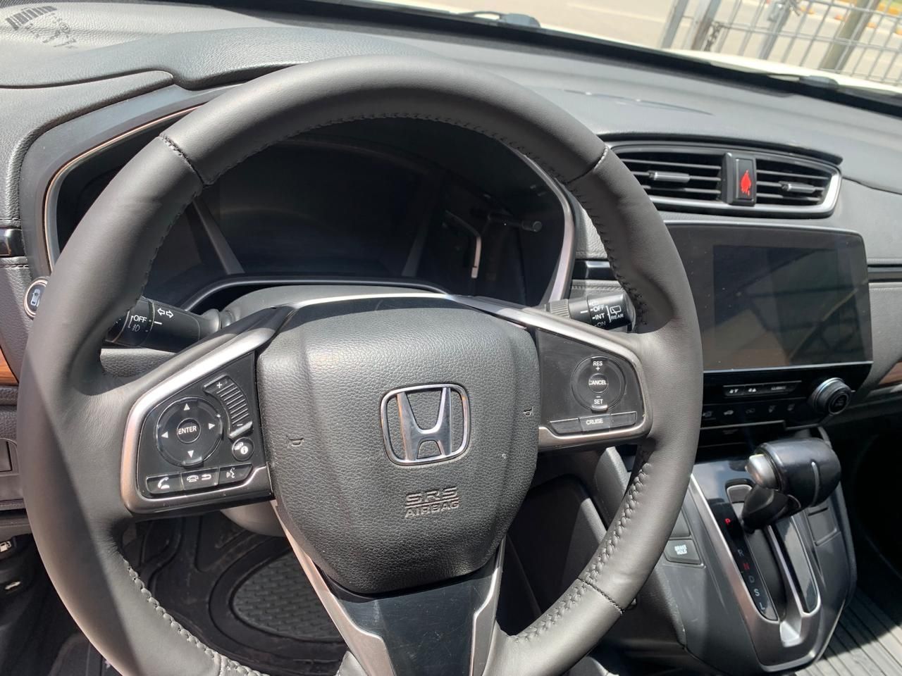 Vista interior del tablero de un Honda CRV, centrándose en el volante, la pantalla de información y entretenimiento y la palanca de cambios.