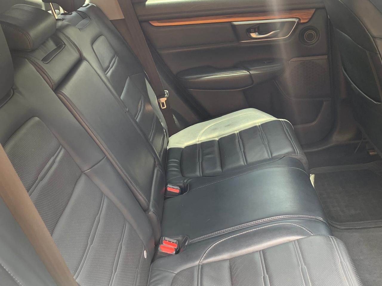 Asiento trasero de automóvil de cuero negro con apoyabrazos central plegado y cinturones de seguridad expuestos.