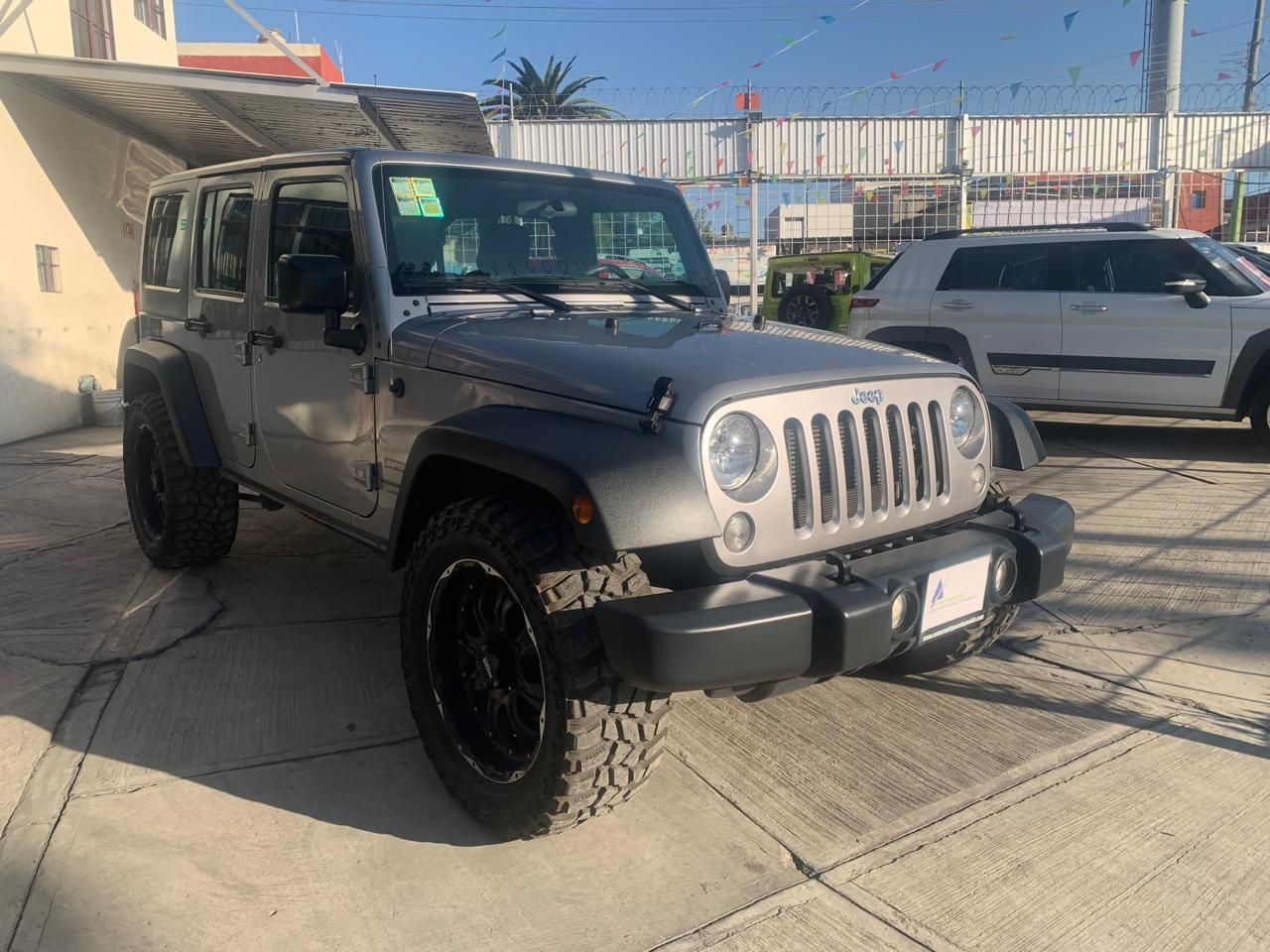 Jeep Wrangler gris estacionado al aire libre con ruedas negras.