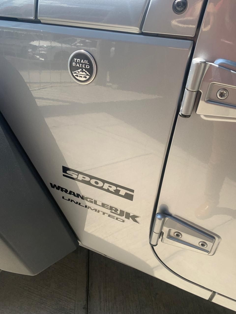 Puerta Jeep Wrangler Sport plateada con insignias.