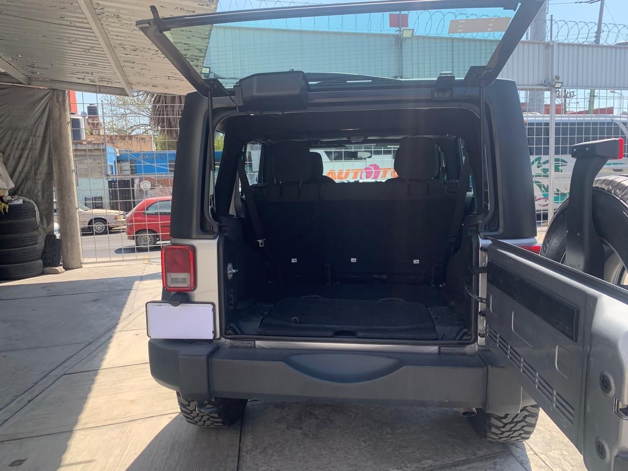 Vista trasera de un Jeep Wrangler plateado con la puerta trasera abierta. Se muestra el área de carga.