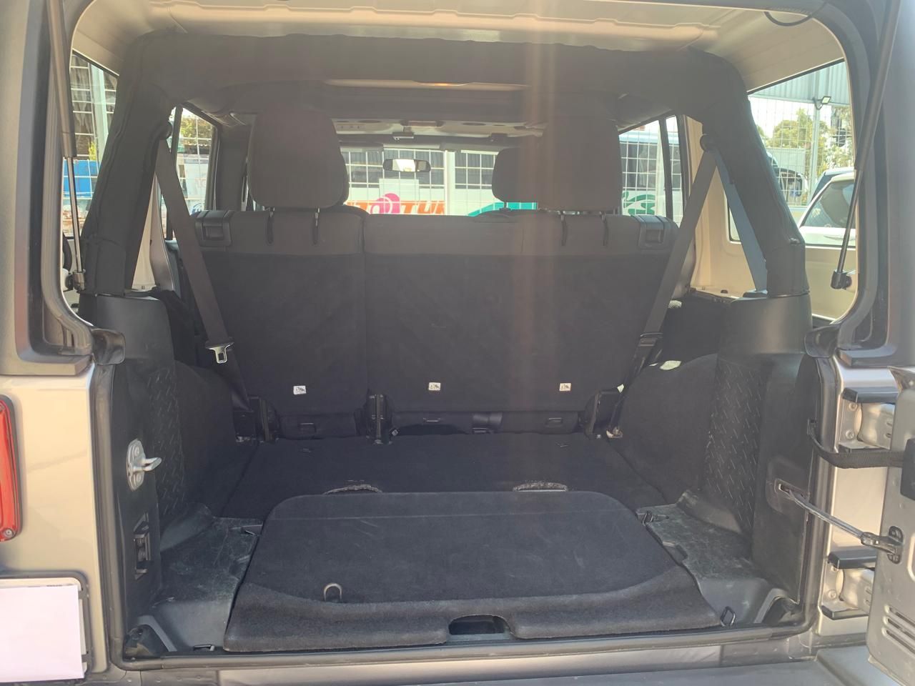 Interior de un Jeep Wrangler: área de carga vacía, asientos traseros levantados, superficies negras, portón trasero abierto.