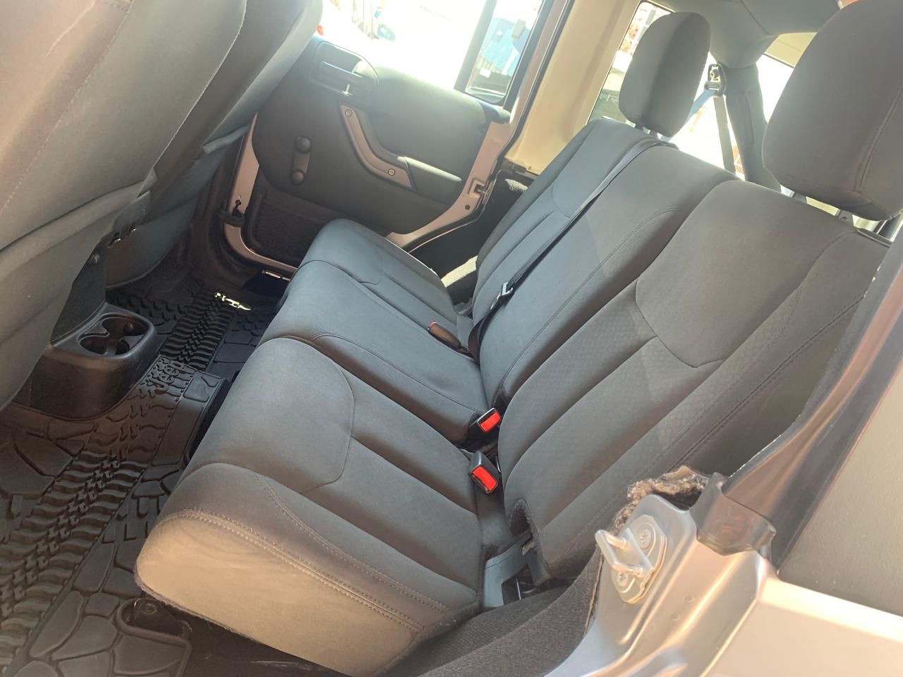 Vista interior del asiento trasero de un Jeep. Asientos de tela gris, alfombrilla negra con dibujo y portavasos.