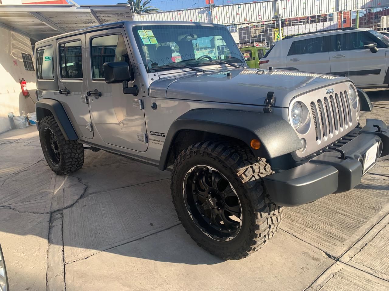 Jeep Wrangler plateado con detalles en negro estacionado al aire libre.
