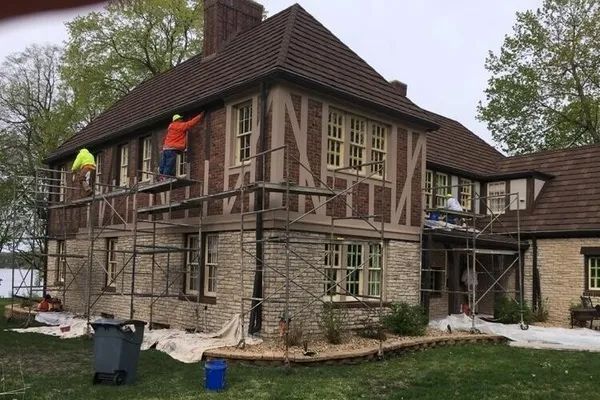 Two men are painting the side of a house with scaffolding.