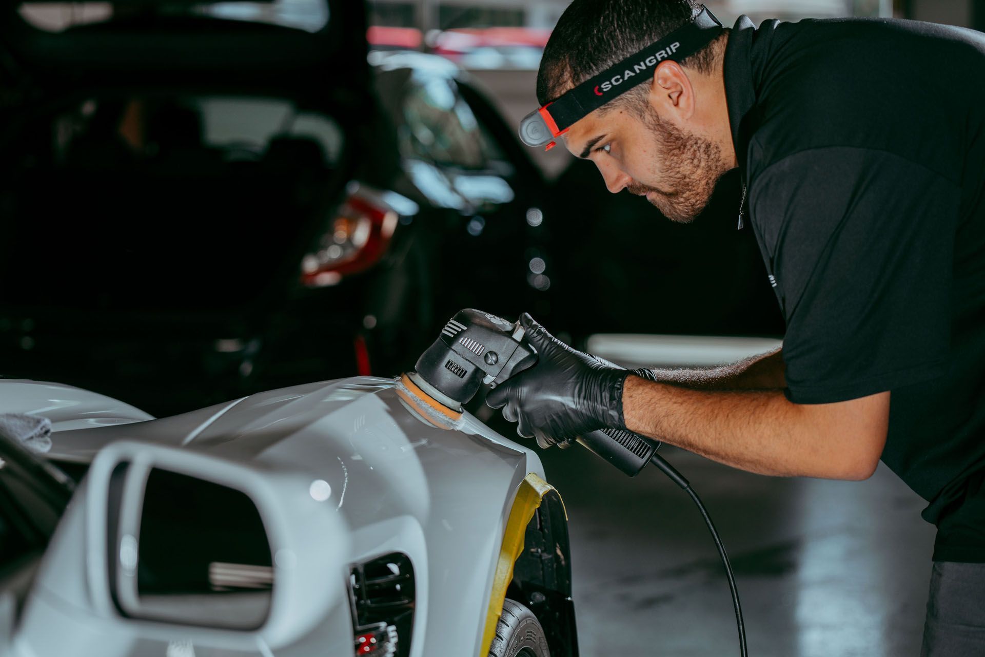 Paint Correction - A man is polishing a car with a sander in a garage .