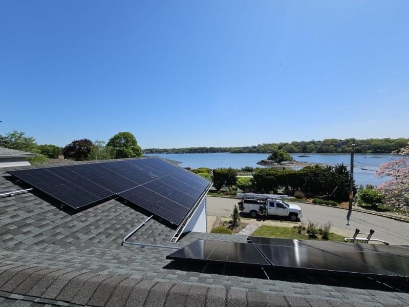 Solar panels on a roof overlooking a sunny waterfront and parked cars