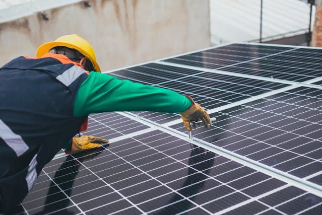 Worker cleaning solar panels on a rooftop, wearing a yellow hard hat and gloves