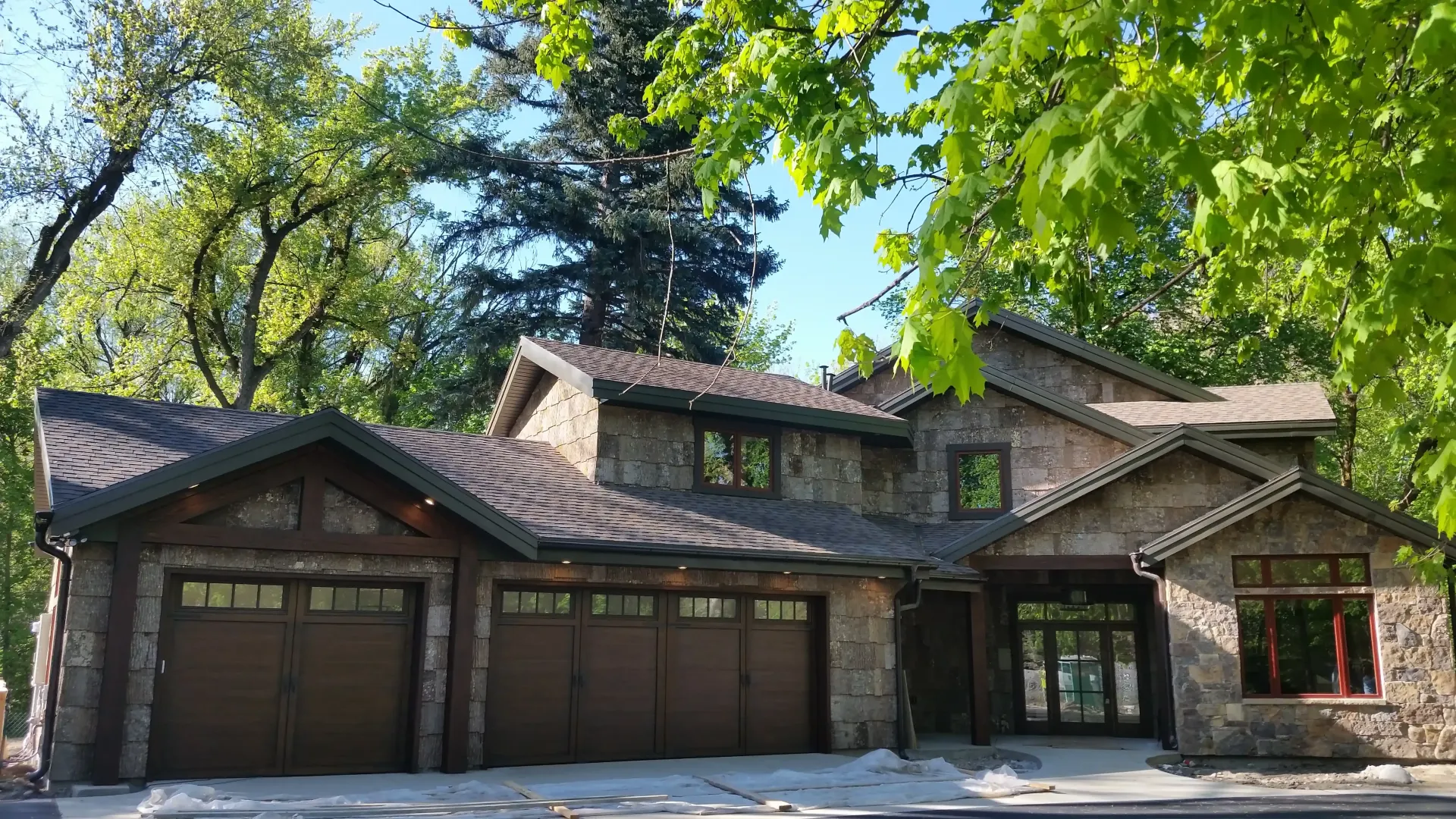 A large house with three garage doors is surrounded by trees.
