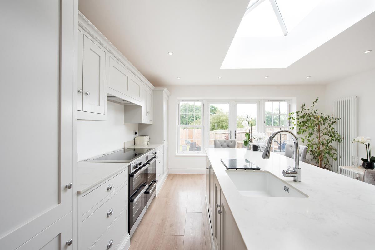 A kitchen with white cabinets , a sink , a stove , and a skylight.