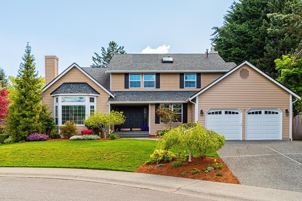 A large house with three garage doors and a lush green lawn.