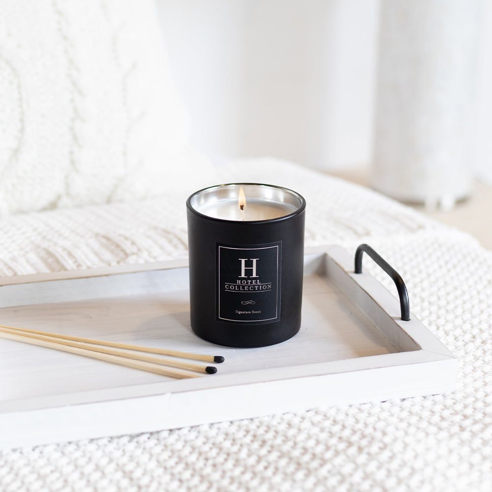 A black candle is sitting on a white tray on a bed.