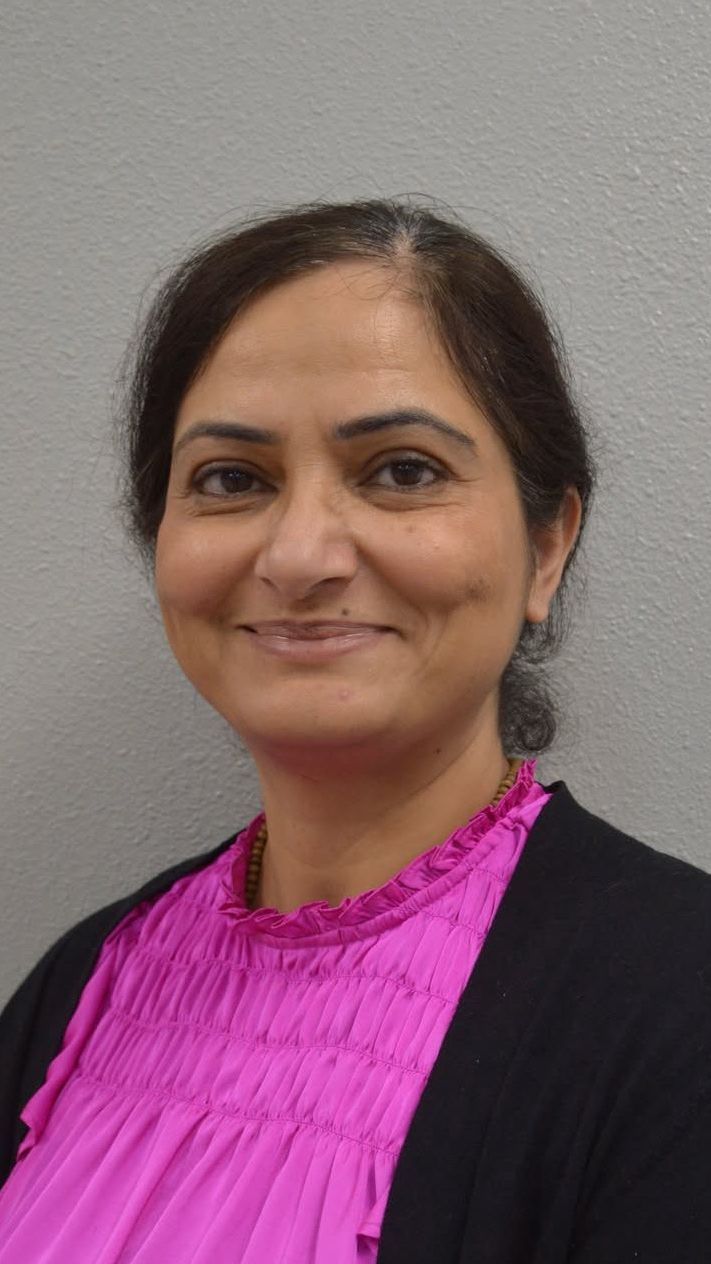 A woman in a pink shirt and black cardigan is smiling for the camera.