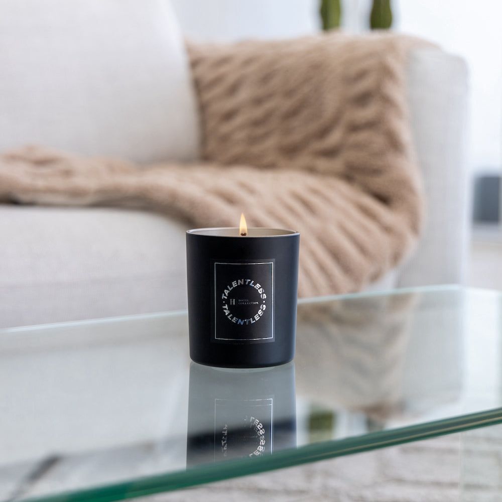 A black candle sits on a glass table in front of a couch