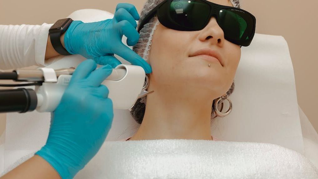 a woman wearing sunglasses is getting a laser treatment on her face .