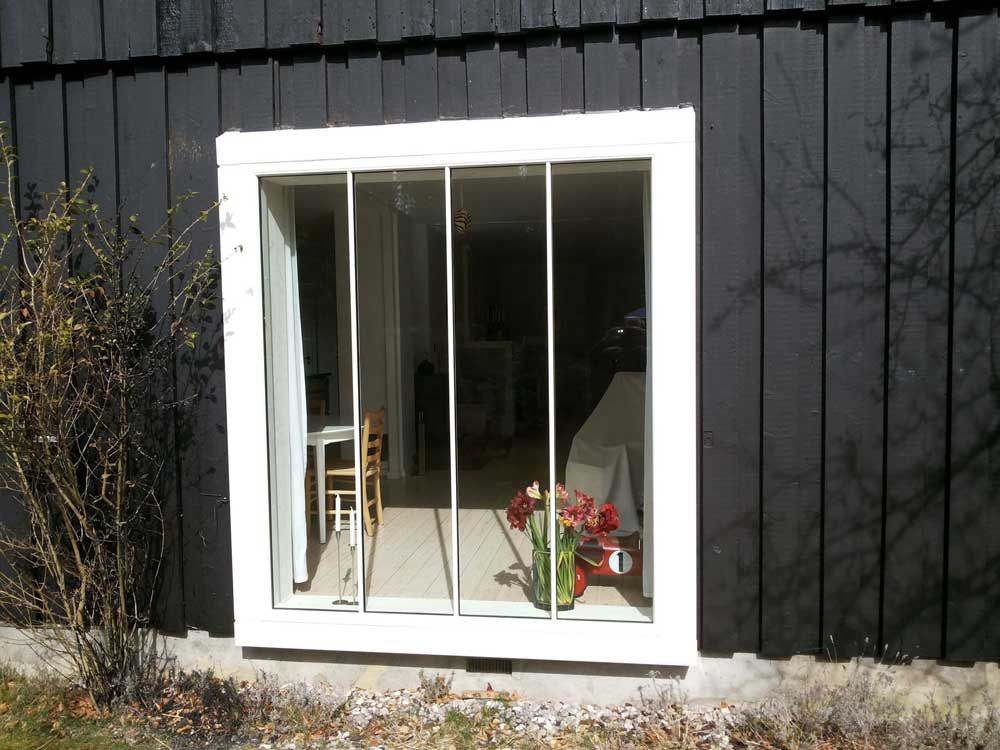 Hvidindrammet vindue i sort trævæg; indvendigt billede med synlige blomster og møbler.