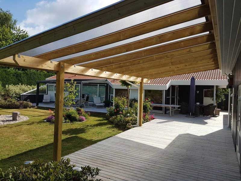 Træpergola over en indkørsel med et hus i baggrunden.