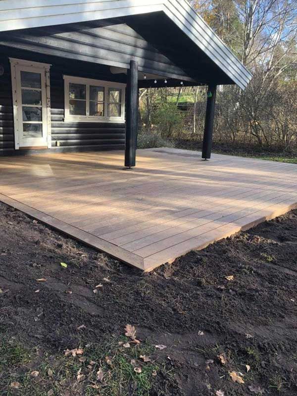 Trædæk med en mørkfarvet kabine og søjler, begravet i jord og blade.