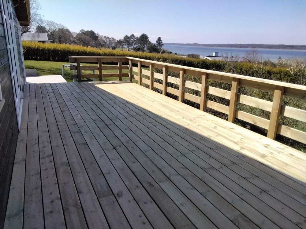Træterrasse med rækværk med udsigt over vand og træer.