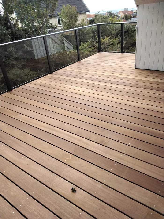 Træterrasse med sort rækværk med udsigt over træer.