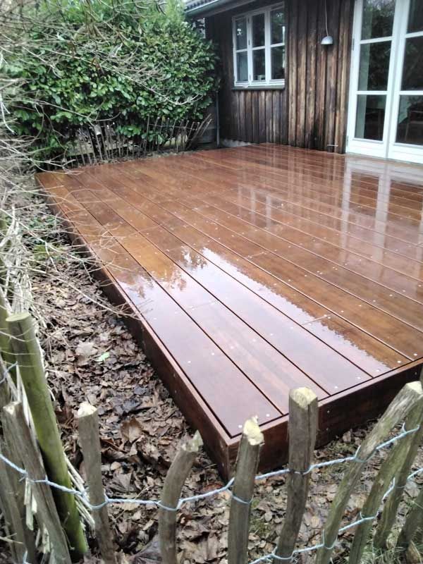 Træterrasse, bejdset brun, ved siden af ​​en bygning og et lille hegn.