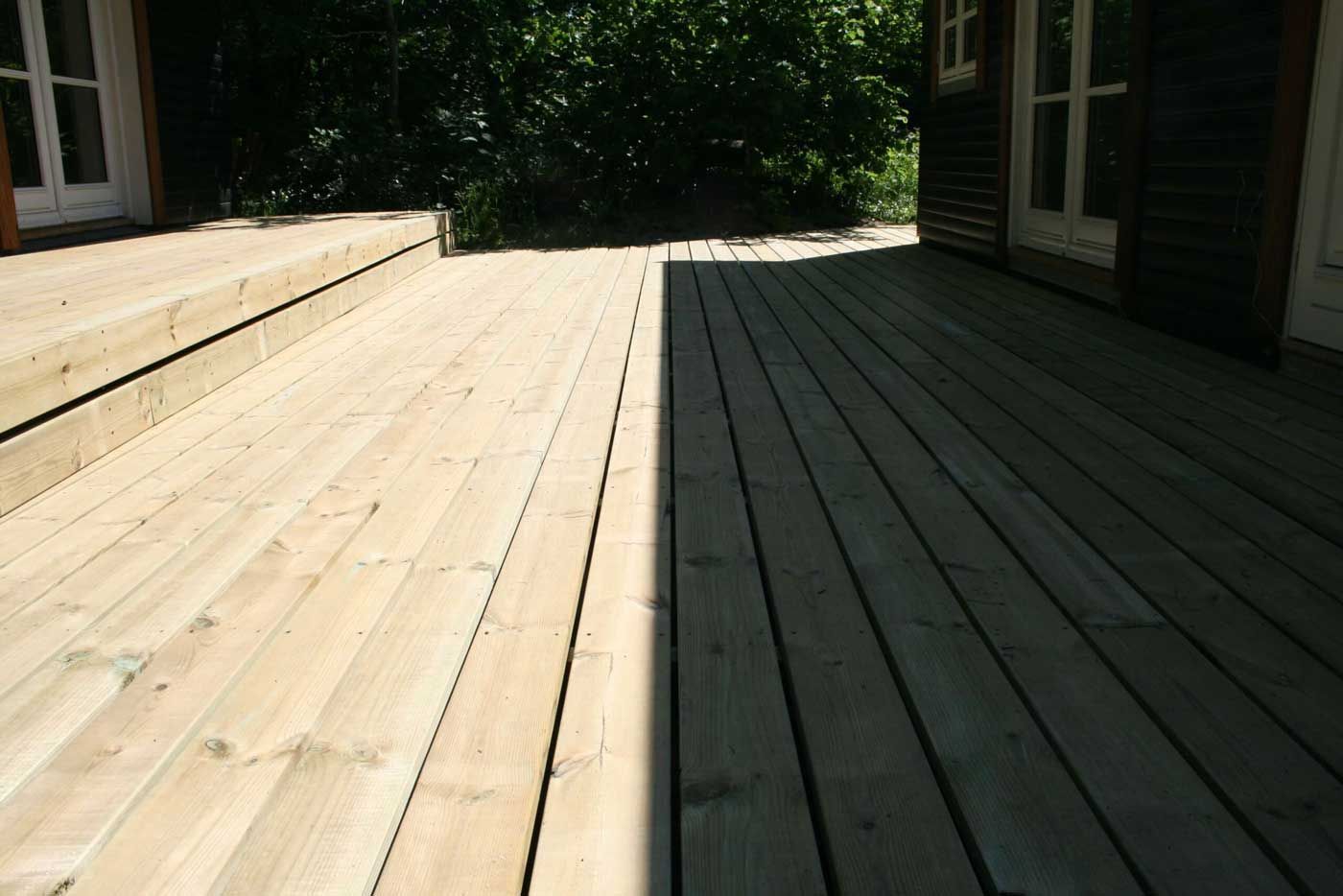 Træterrasse, halvt i sollys, ved siden af ​​en bygning med døre.