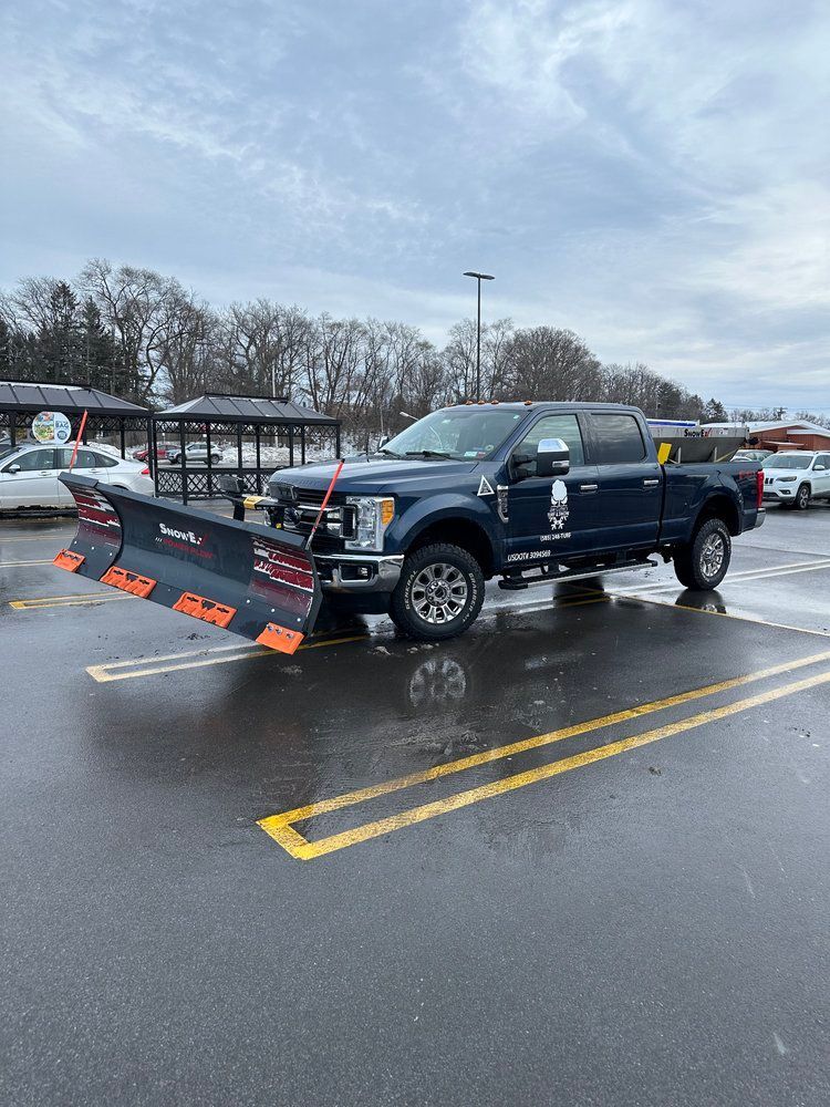 A blue truck with a snow plow attached to it is parked in a parking lot.