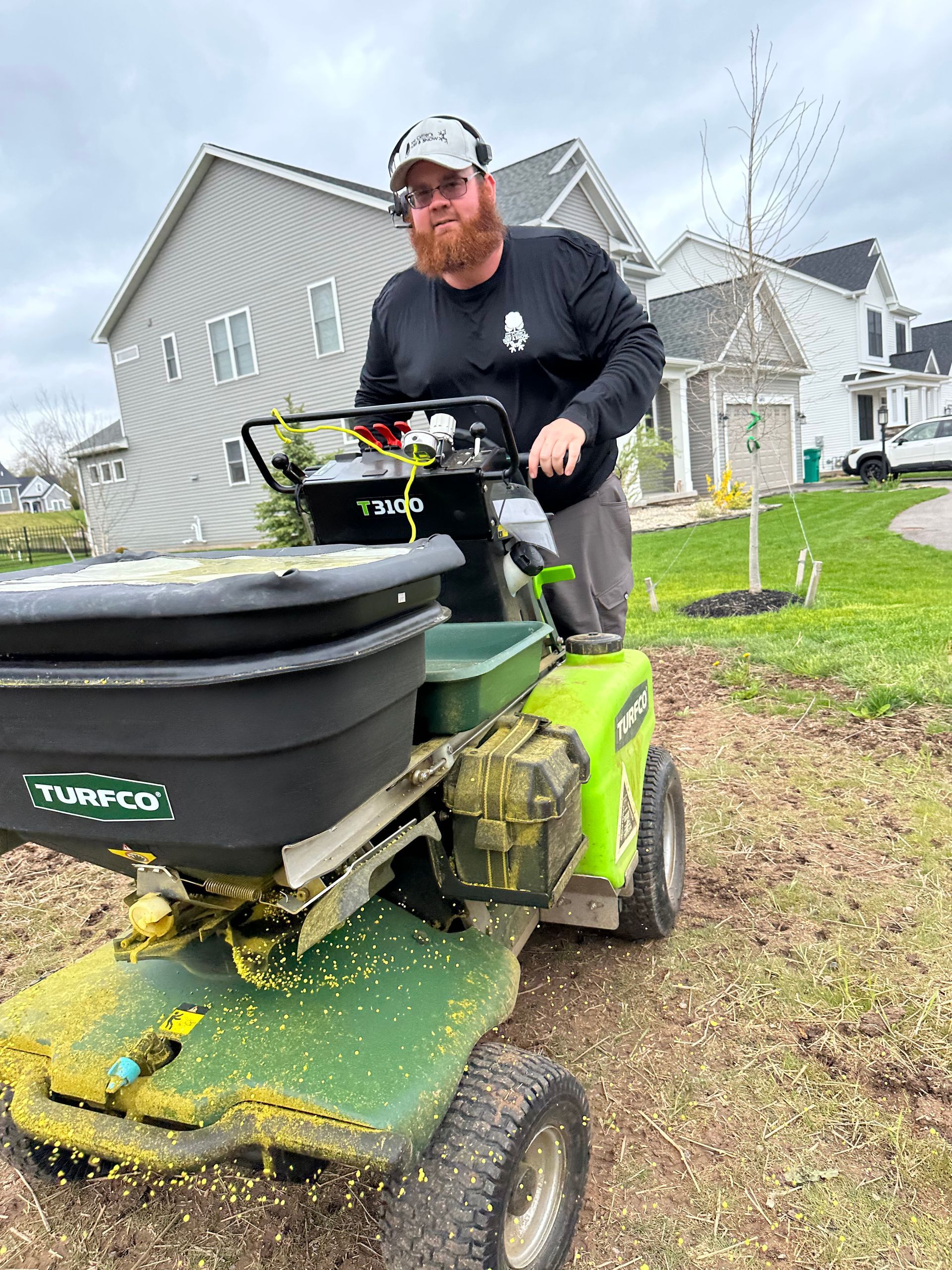 A person is spreading fertilizer on a lawn with an earthway spreader