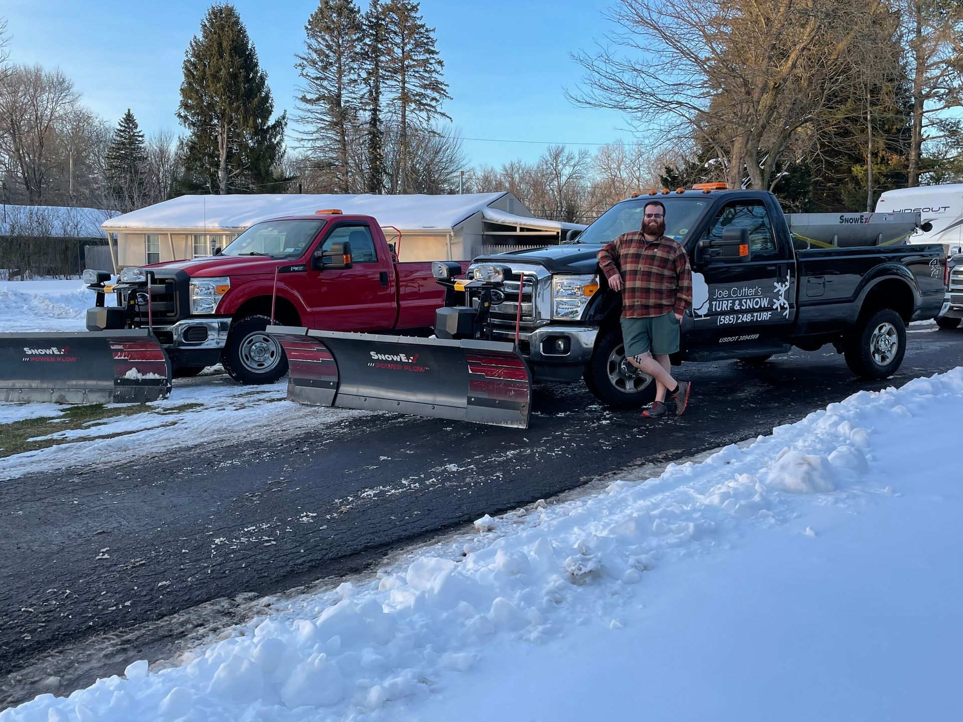 A man is standing next to two snow plows on the side of the road.