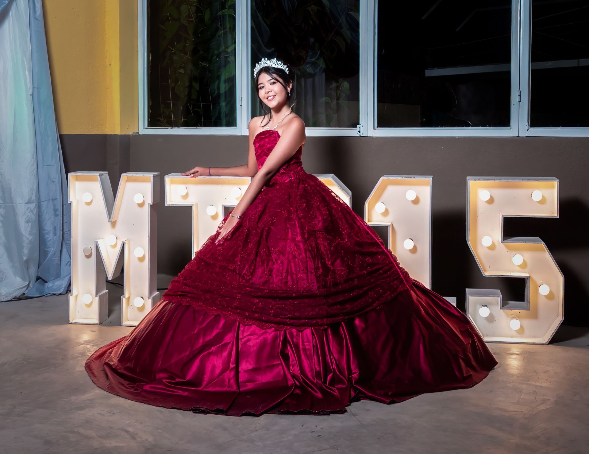 Mujer con un vestido de gala color burdeos posando junto a grandes letras iluminadas en el telón de fondo de un evento.