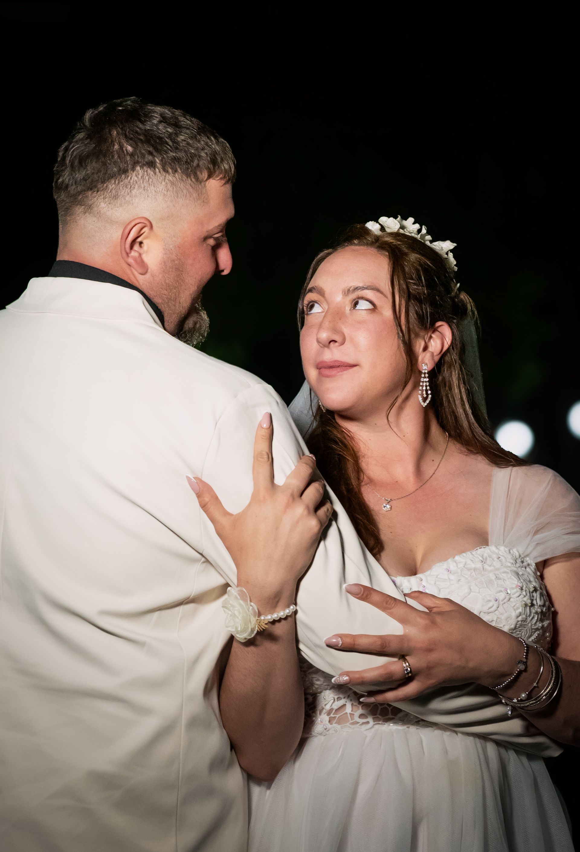 Pareja bailando de noche, la mujer con vestido blanco mira hacia arriba a un hombre con chaqueta blanca, sonriendo.