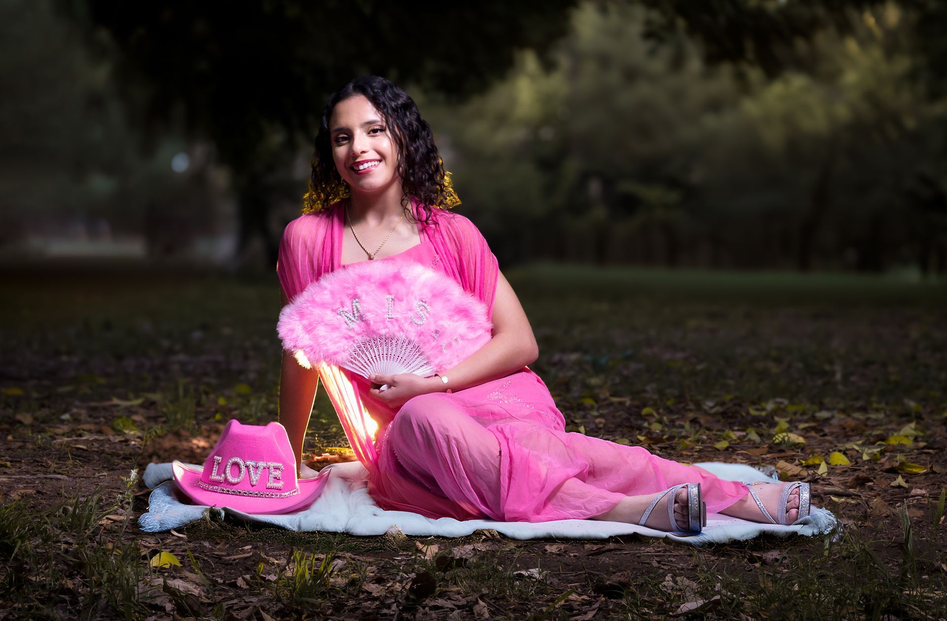 Una mujer con un vestido rosa sentada sobre una manta al aire libre, sosteniendo un ramo de flores.