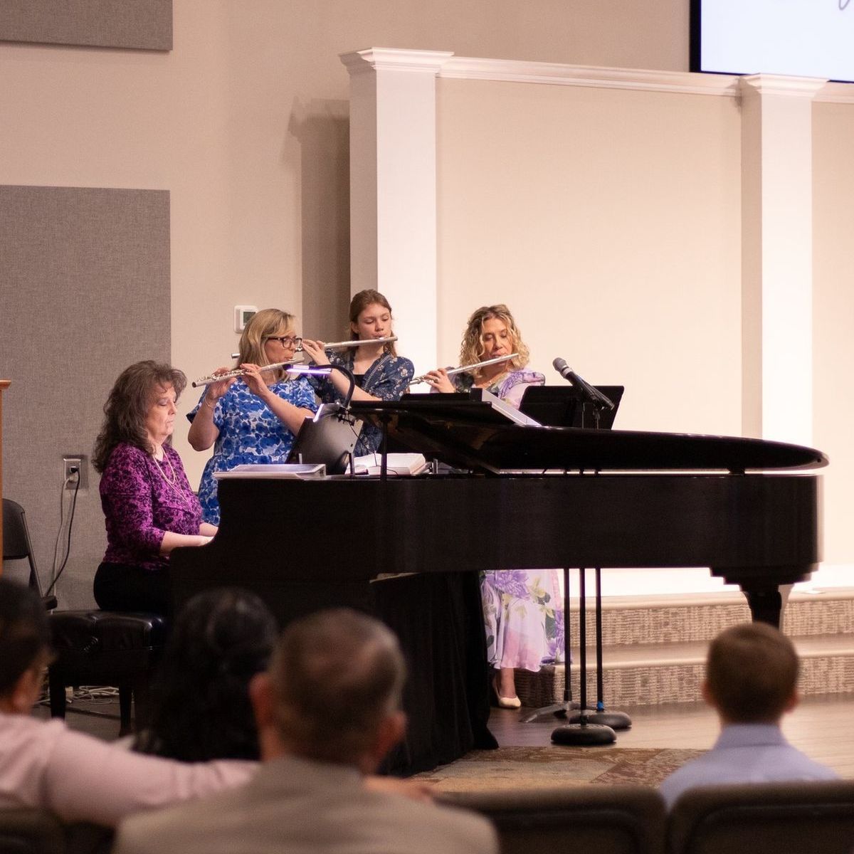 Four women play flutes with a piano in a church.