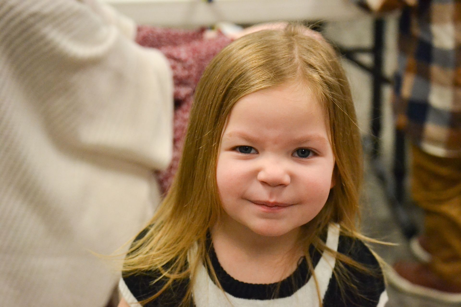 Blonde-haired girl in a striped top; looking at the camera, slight smirk.