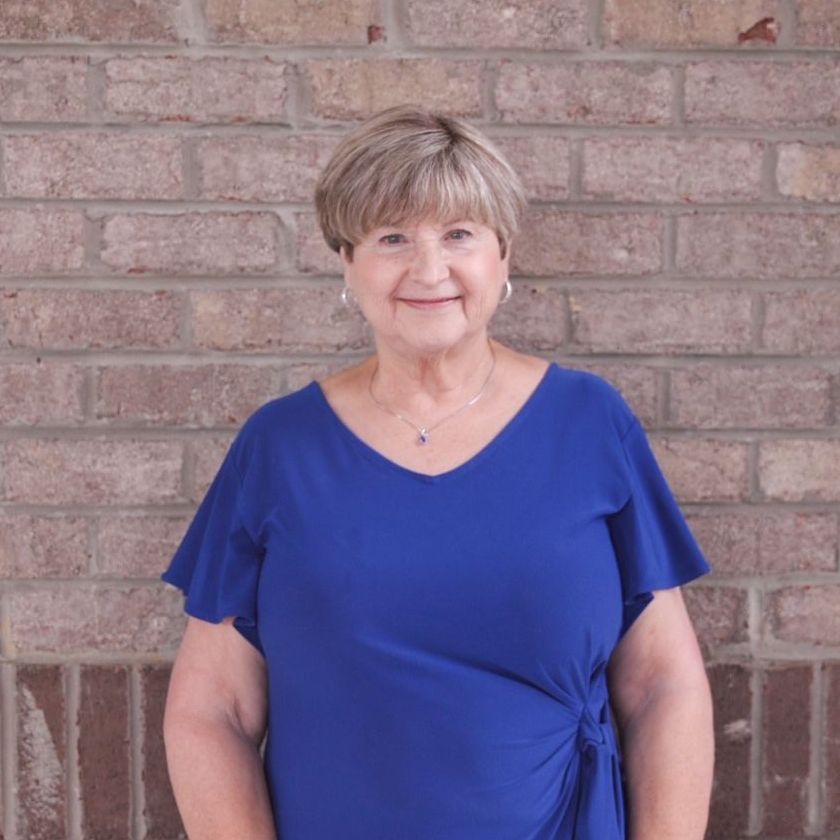 A woman in a blue shirt is standing in front of a brick wall.