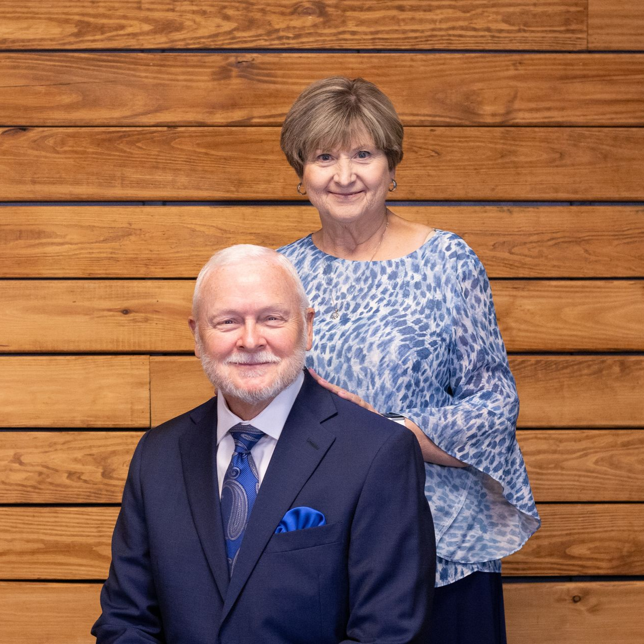 Pastor David and Vickie Shaffer standing in front of a building; woman in blue shirt and skirt, man in blue shirt and slacks.