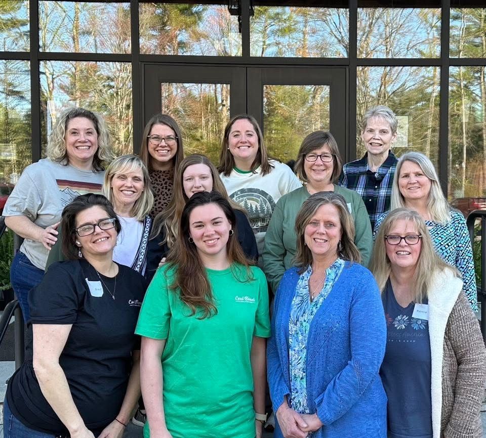 Group of women smiling outside a building with large windows. Some wear green, blue, and patterned tops.