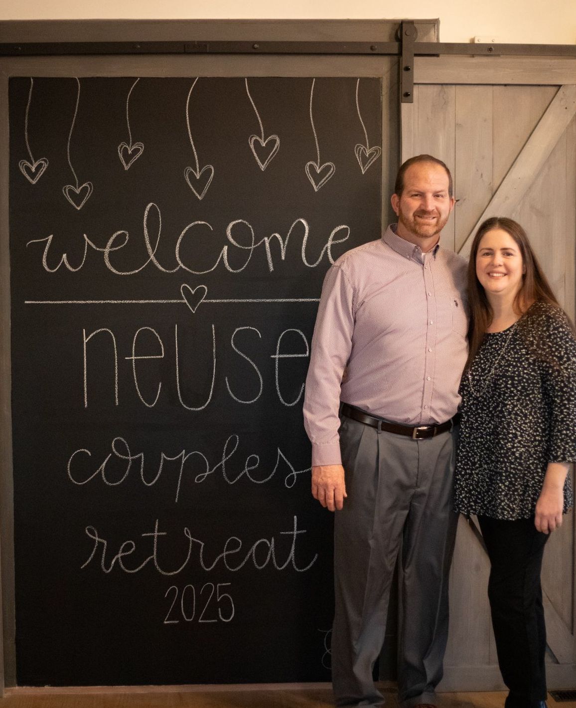 Couple stands in front of a chalkboard sign that reads