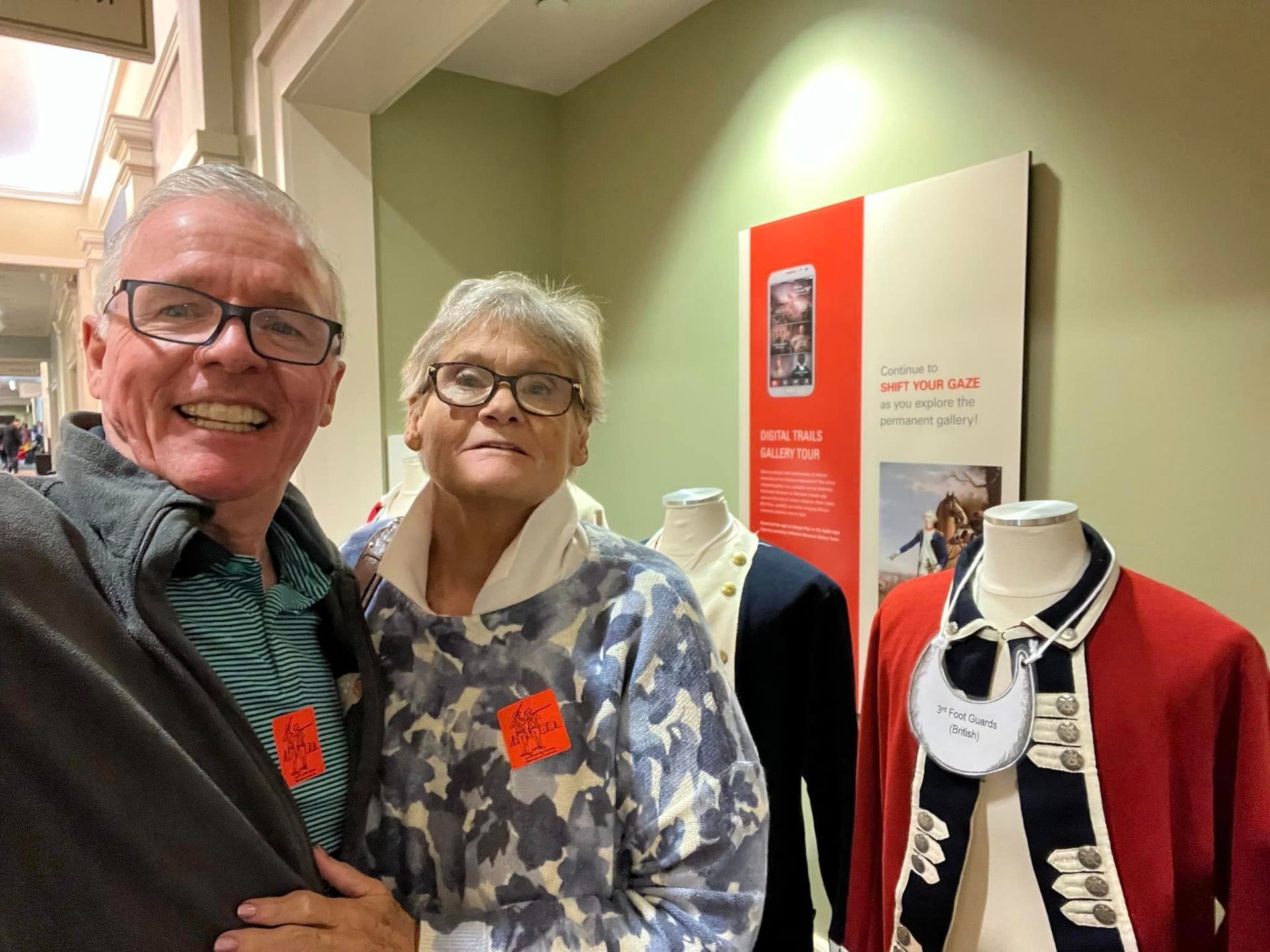 Couple smiles at museum exhibit with display of red jacket and necktie.